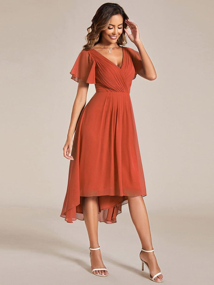 Seitlich fotografiertes terrakottafarbenes Kleid, Model lächelt und berührt ihr Haar, der asymmetrische Chiffonsaum schwingt mit. 96