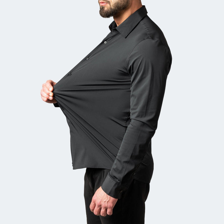 Mann im schwarzen Hemd zieht den Stoff am Bauch seitlich weit nach vorn und zeigt so die starke Dehnbarkeit. 2