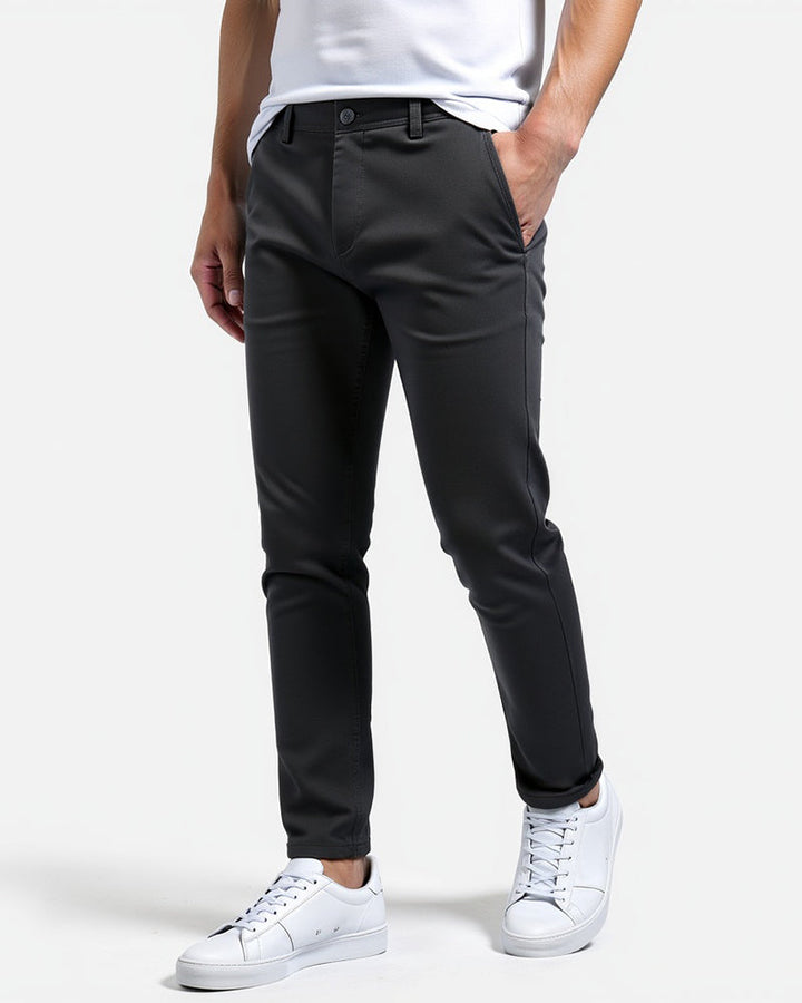 Dunkelgraue Chino in Seitenansicht mit hochgekrempeltem Saum, getragen mit weißem T-Shirt und weißen Sneakern, Hand in der Tasche. 6