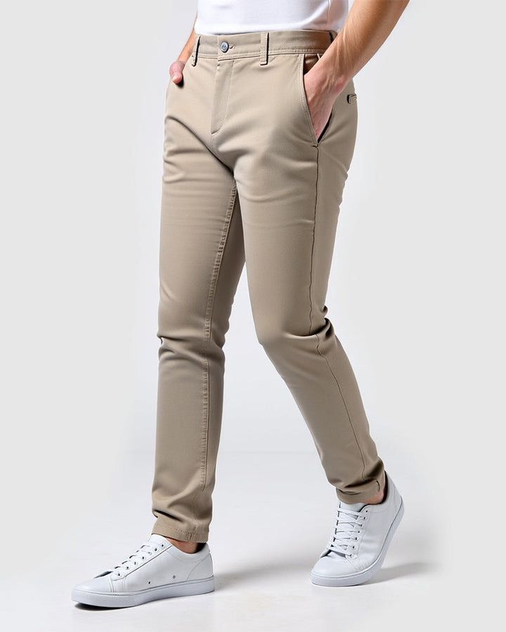Beige Chino in Seitenansicht mit weißem T-Shirt und weißen Sneakern, beide Hände in den Hosentaschen. 14