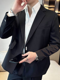 Mann im eleganten schwarzen Anzug mit weißem Hemd, hält Smartphone, trägt Armbanduhr und Ringe.