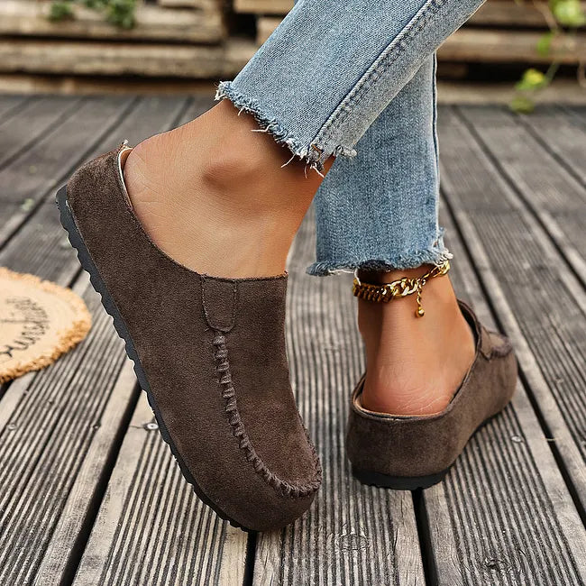 Dunkelbraune Slipper beim Gehen, seitlich und von hinten gezeigt, mit offener Ferse und dünner schwarzer Sohle. 6