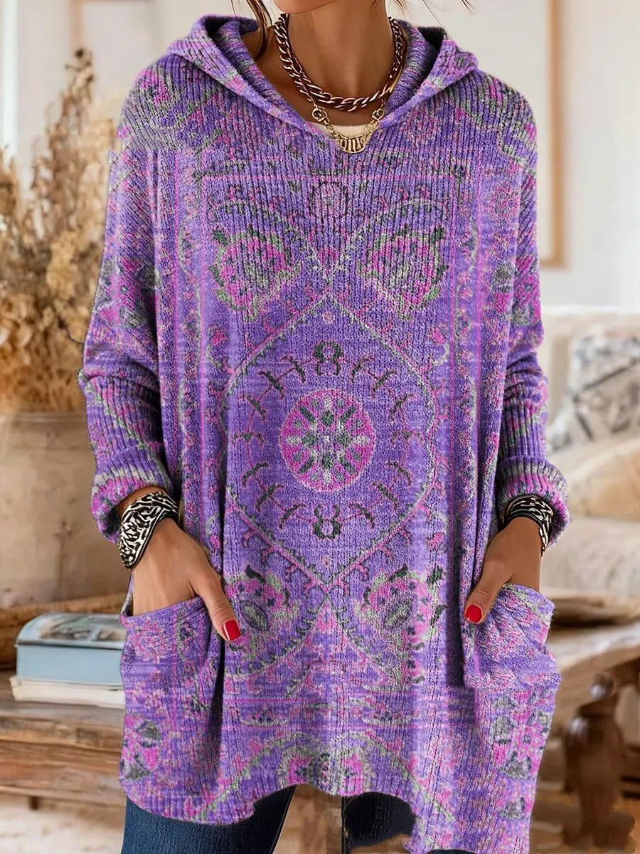 Getragene Kapuzentunika in Violett mit rosa und grünem Ornamentmuster, Hände in den großen Vordertaschen, Nahaufnahme von Oberkörper und Saum. 2