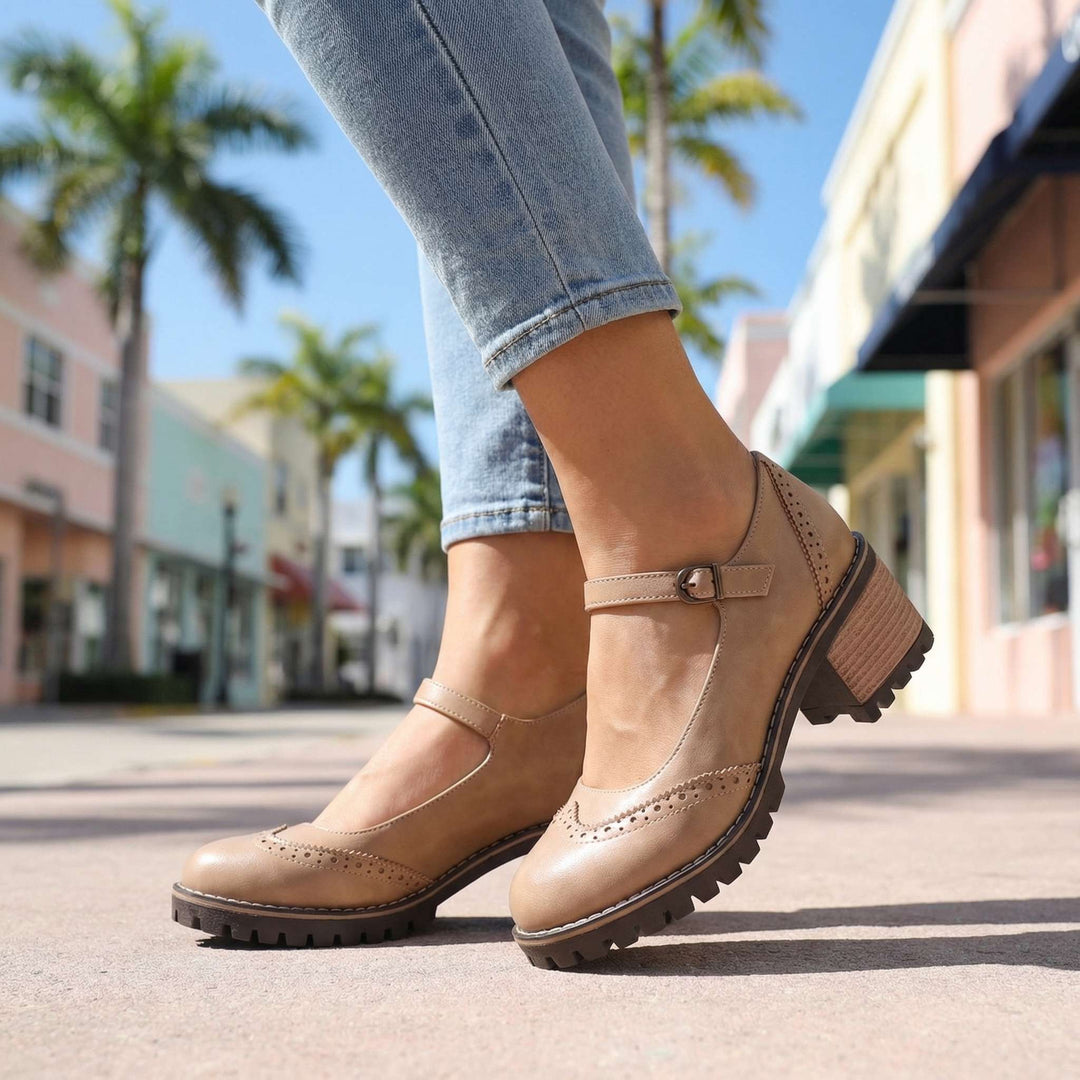 Beige Mary Janes in Untersicht, mit Riemen, Schnalle und Blockabsatz, getragen zu Jeans vor Palmen und bunten Geschäftsfassaden. 9
