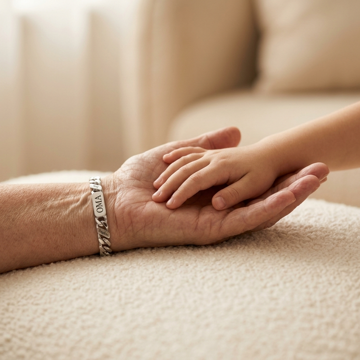 Die Hand einer älteren Person mit silberfarbenem Gliederarmband hält die kleine Hand eines Kindes auf einer weichen cremefarbenen Decke. 5