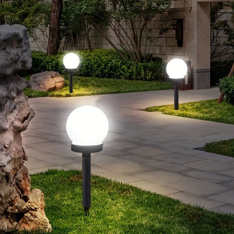 Leuchtende Gartenkugellampen auf Rasenweg, moderne Außenbeleuchtung, energiesparend.