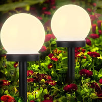 Zwei kugelförmige Solarleuchten im Garten, umgeben von roten Blumen, leuchten nachts.