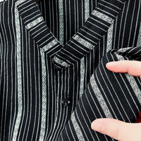 Schwarz-weiß gestreiftes Hemd aus Baumwolle, Nahaufnahme, Hand hält Stoff, modisches Design.