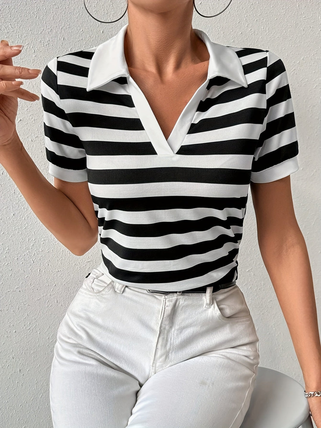 Frau trägt schwarz-weiß gestreiftes Poloshirt, V-Ausschnitt, weiße Hose, modisch, elegant.
