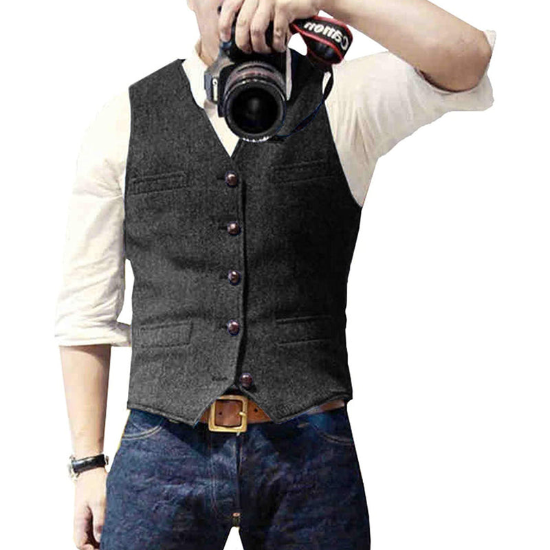 Mann mit grauem Wollweste, weißem Hemd, Jeans, hält Kamera.