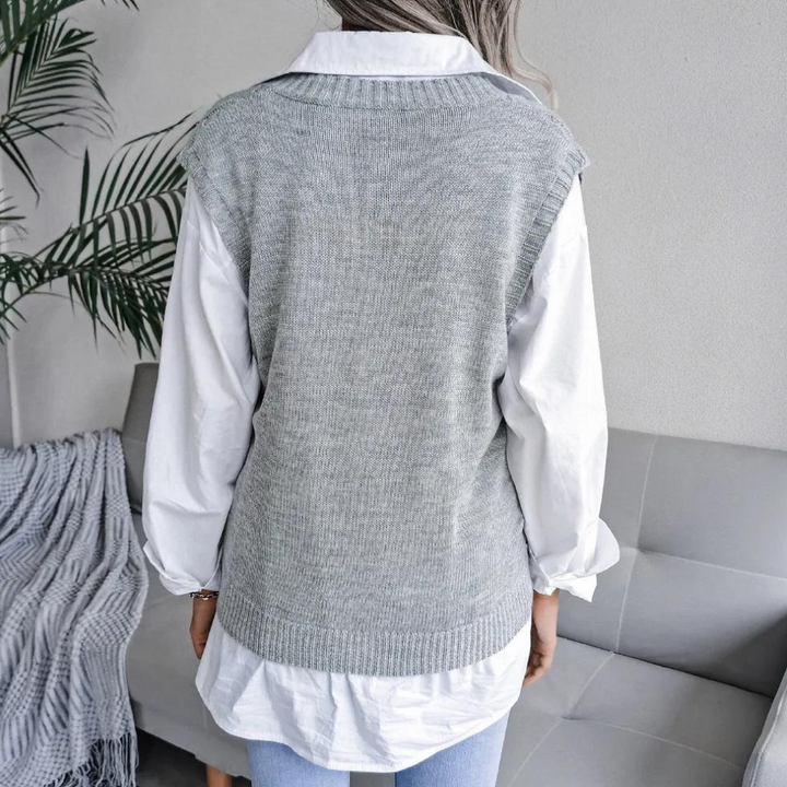 Frau in grauem Strickpullunder über weißer Bluse, moderne Mode, gemütliches Wohnzimmer.
