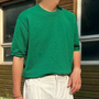 Mann in grünem T-Shirt und weißen Hosen vor Holzhaus, Sommermode, Freizeitkleidung.