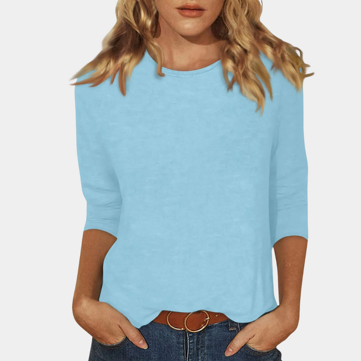 Frau in hellblauem Langarmshirt, Jeans, brauner Gürtel, blonde Haare.
