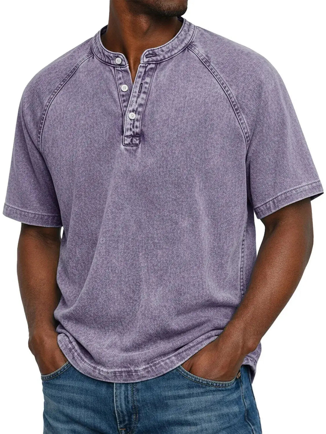 Mann trägt das Henley-Shirt mit Raglanärmeln und Knopfleiste in verwaschenem Flieder, Hände in den Jeanstaschen, Frontansicht. 1