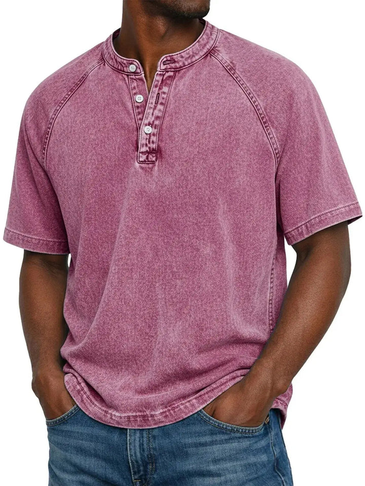 Mann trägt das Henley-Shirt mit Raglanärmeln und Knopfleiste in verwaschenem Rosa-Beerenton zu blauer Jeans, Frontansicht. 10