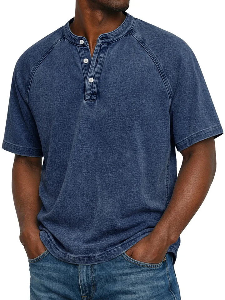 Mann trägt das Henley-Shirt mit Raglanärmeln und Knopfleiste in verwaschenem Dunkelblau zu blauer Jeans, Frontansicht. 3