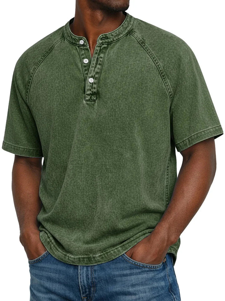 Mann trägt das Henley-Shirt mit Raglanärmeln und drei Knöpfen in verwaschenem Dunkelgrün zu Jeans, Frontansicht. 7