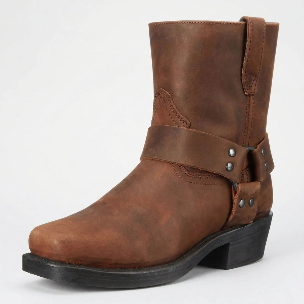Brauner Lederstiefel mit genietetem Zierriemen, eckiger Spitze und schwarzem Absatz, schräg von vorn vor hellem Hintergrund. 2