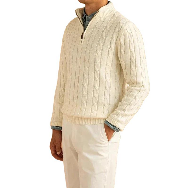 Mann trägt den cremeweißen Zopfstrick-Pullover mit offenem Reißverschluss über einem Hemd, dazu helle Hose, Hand in der Hosentasche. 1