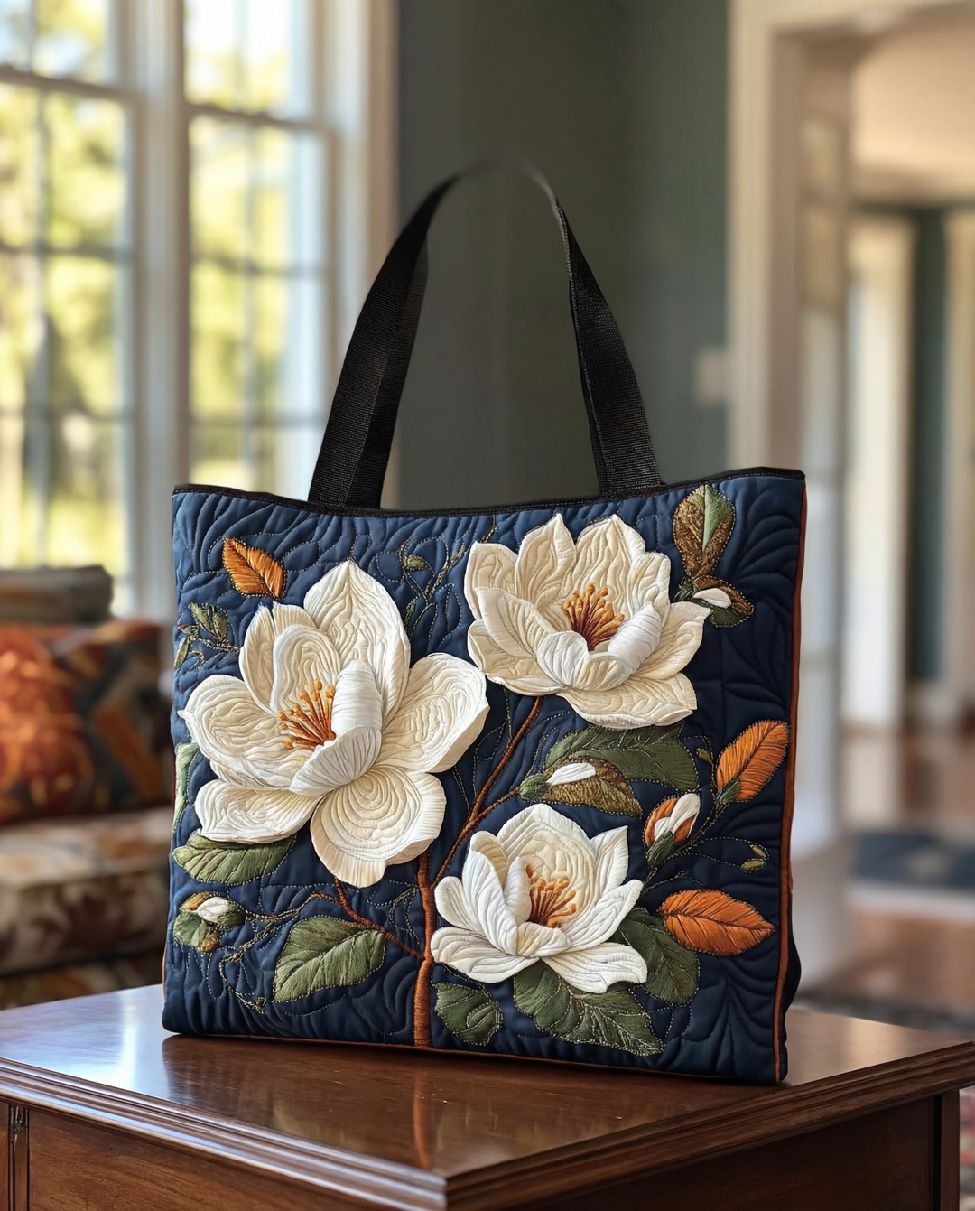 Dunkelblaue gesteppte Tragetasche mit schwarzen Henkeln und plastisch aufgestickten weißen Magnolienblüten, auf einem Holztisch im Wohnzimmer stehend. 1
