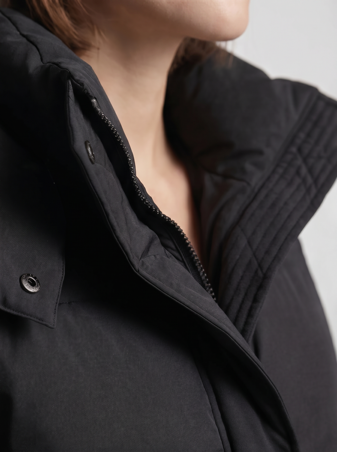 Detailaufnahme von Stehkragen, Reißverschluss, Druckknopf und Steppnähten der schwarzen Jacke am Model 7