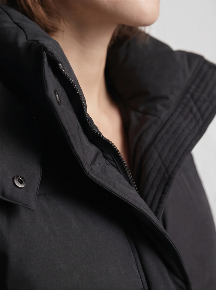 Detailaufnahme von Stehkragen, Reißverschluss, Druckknopf und Steppnähten der schwarzen Jacke am Model 7