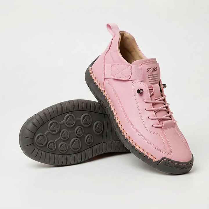 Rosa Sneaker mit orangefarbener Handnaht und dunkelgrauer Sohle, daneben ein Schuh mit sichtbarer Noppensohle. 14