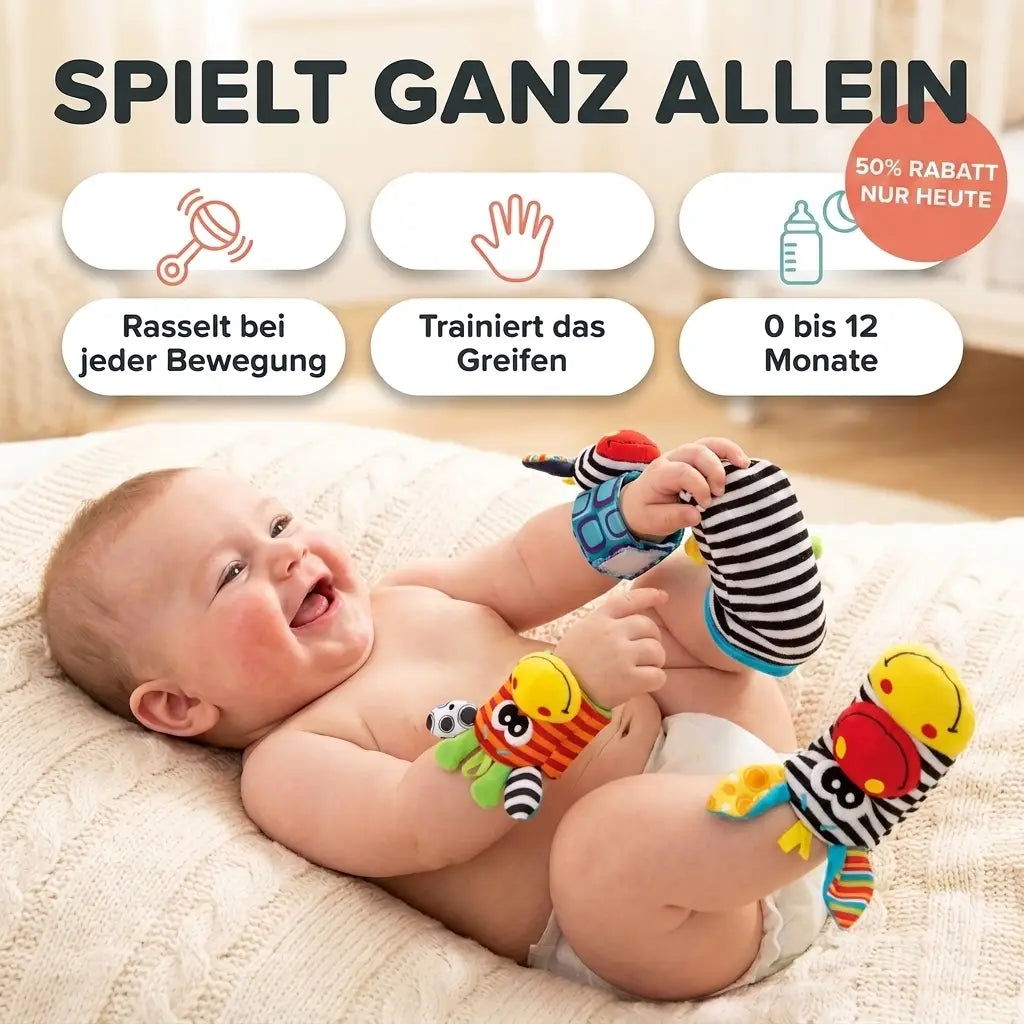 Lachendes Baby liegt auf einer Strickdecke und trägt Rasselbänder am Handgelenk und gestreifte Rasselsocken an den Füßen. 1