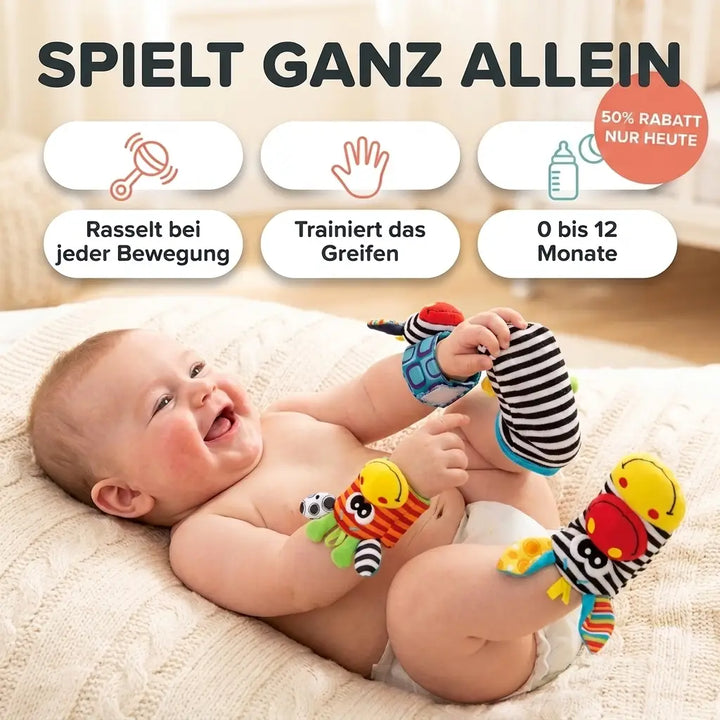 Lachendes Baby liegt auf einer Strickdecke und trägt Rasselbänder am Handgelenk und gestreifte Rasselsocken an den Füßen. 1