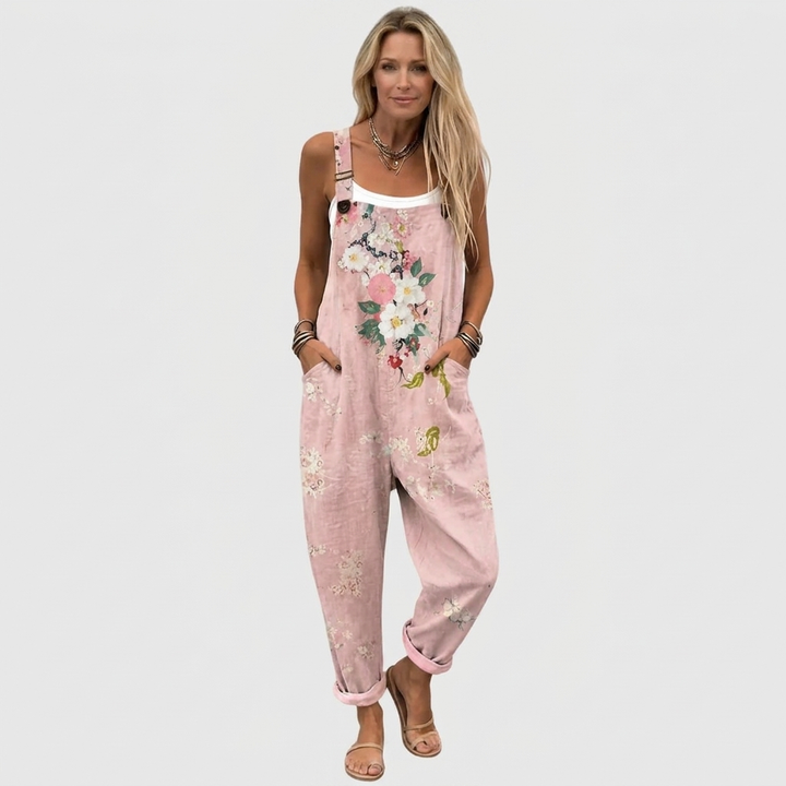 Frontansicht in Ganzkörperaufnahme: Model mit weißem Top unter der Latzhose, Blumenmuster, hochgekrempelte Beine und Sandalen. 2