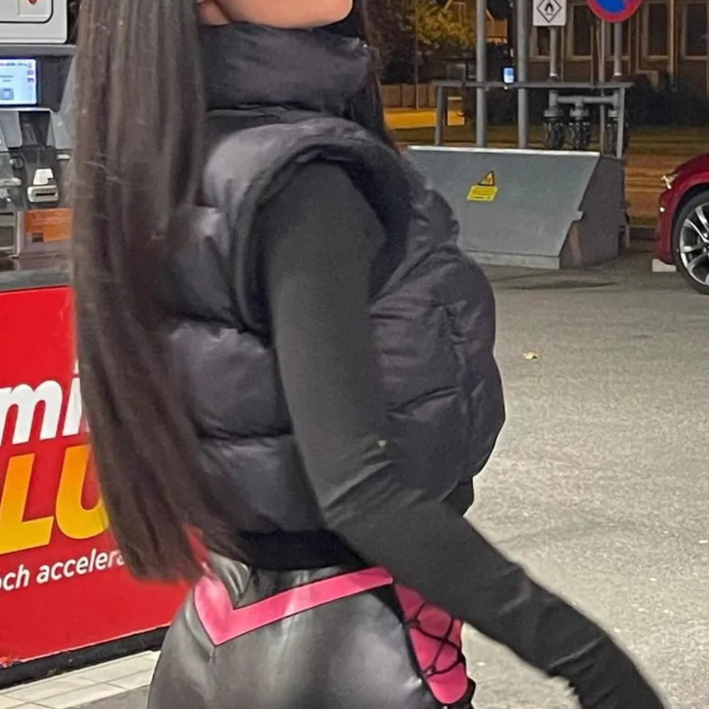 Schwarze Daunenweste, schwarze Lederhose, Frau an Tankstelle, Nachtaufnahme.