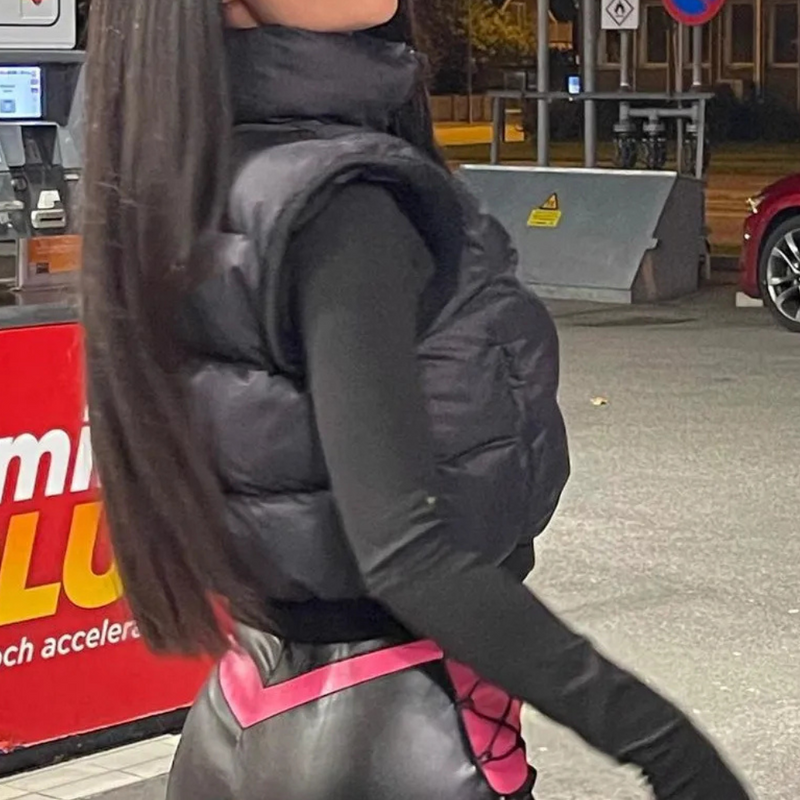 Schwarze Daunenweste, schwarze Lederhose, Frau an Tankstelle, Nachtaufnahme.