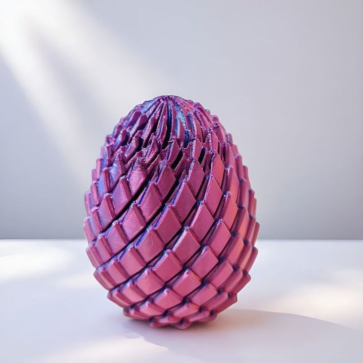 Drachenei in glänzendem Violett-Pink auf weißer Fläche, seitlich von Sonnenlicht und Schatten gestreift. 10