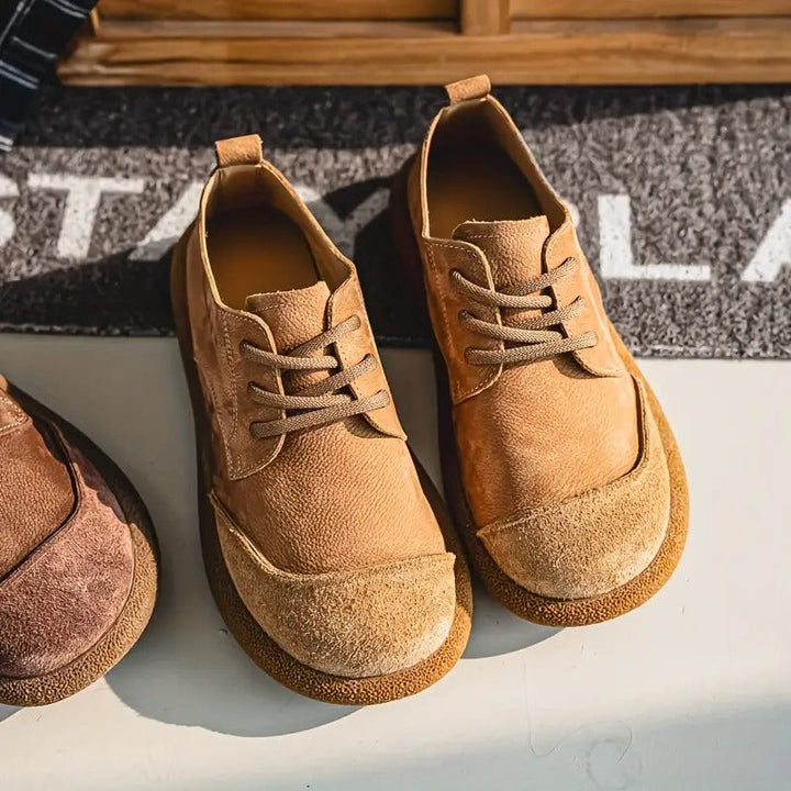 Hellbraune Schnürschuhe mit heller Wildlederkappe schräg von oben auf einer hellen Fläche vor einer grauen Fußmatte. 2