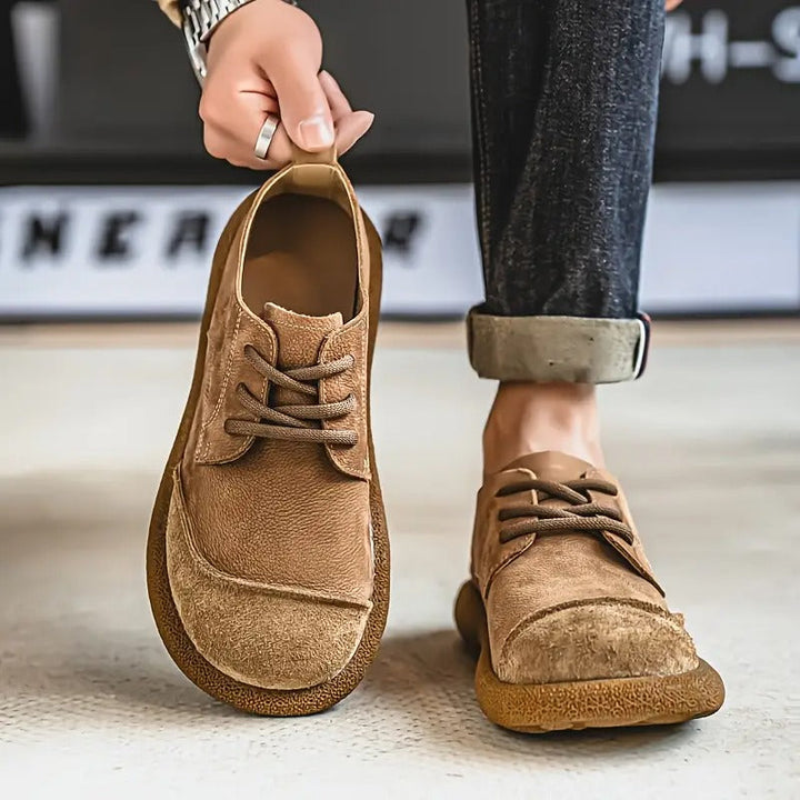 Ein Schuh wird an der Anziehlasche hochgehalten, der andere Schuh wird mit hochgekrempelter Jeans getragen; hellbraune Ausführung. 3