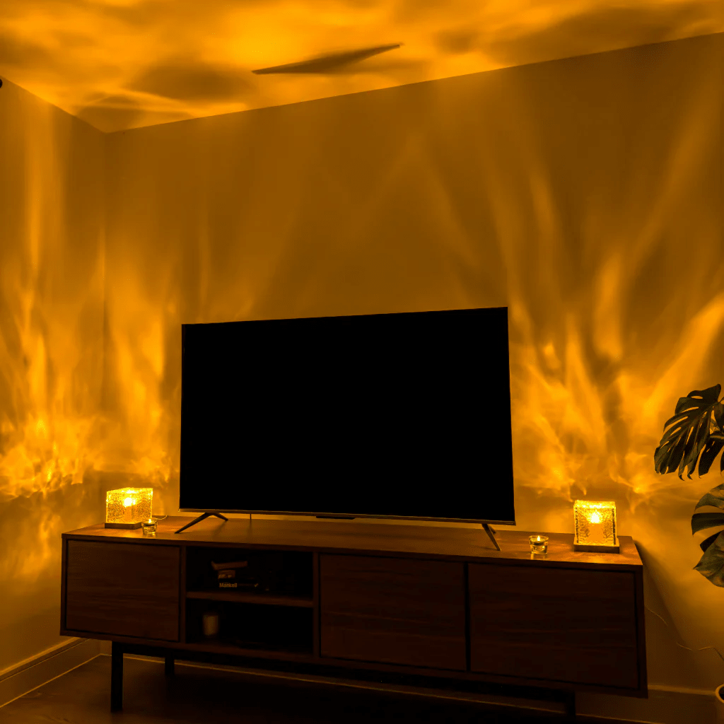 Zwei leuchtende Würfellampen auf einem Sideboard unter einem Fernseher werfen goldgelbe, flammenartige Lichtmuster an die Wand. 4