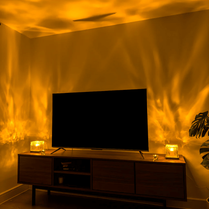 Zwei leuchtende Würfellampen auf einem Sideboard unter einem Fernseher werfen goldgelbe, flammenartige Lichtmuster an die Wand. 4
