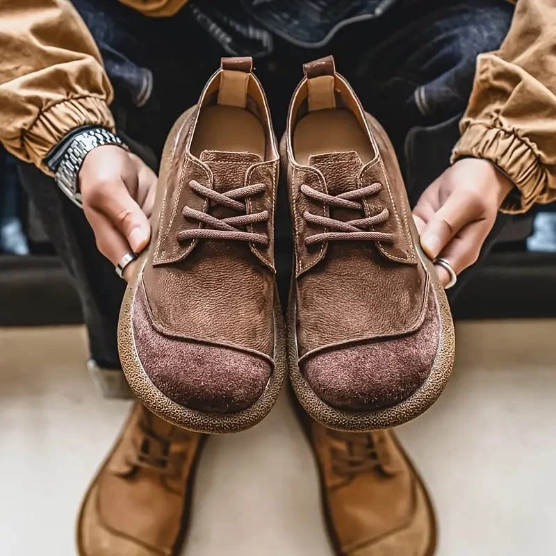 Zwei Hände halten ein Paar dunkelbraune Schnürschuhe von vorn, darunter stehen hellbraune Schuhe an den Füßen. 10