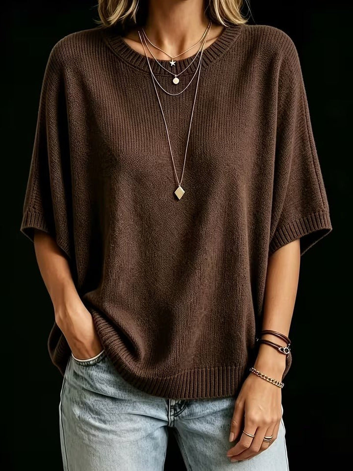 Dunkelbraunes Strickoberteil mit Rundhals und gerippten Bündchen, getragen mit Halsketten, Armbändern und einer Hand in der Jeanstasche. 19