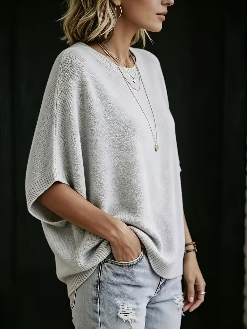 Seitenansicht des hellgrauen Strickoberteils mit weiten Fledermausärmeln, getragen mit Jeans und Hand in der Hosentasche. 2