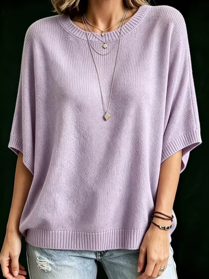 Frontansicht des fliederfarbenen Strickoberteils mit locker fallenden Fledermausärmeln, getragen mit Halsketten und Lederarmbändern. 10