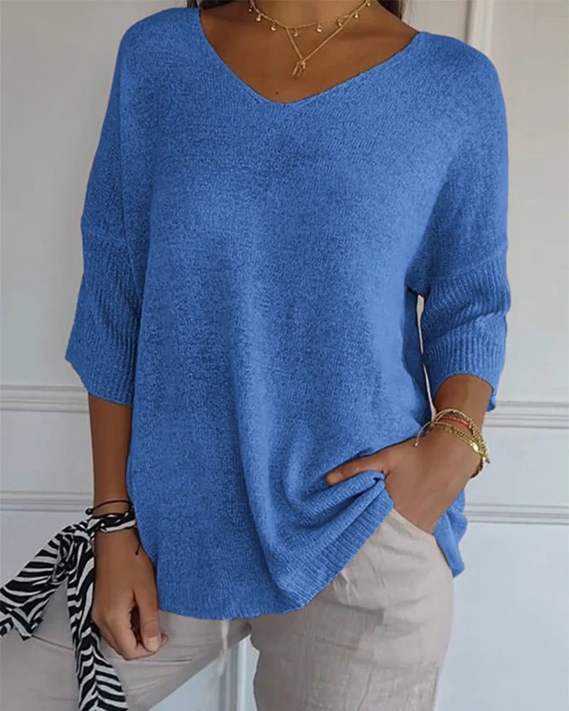 Frau trägt den blauen Strickpullover locker zu hellen Leinenhosen, mit Goldketten und Armbändern, Hand in der Tasche 1