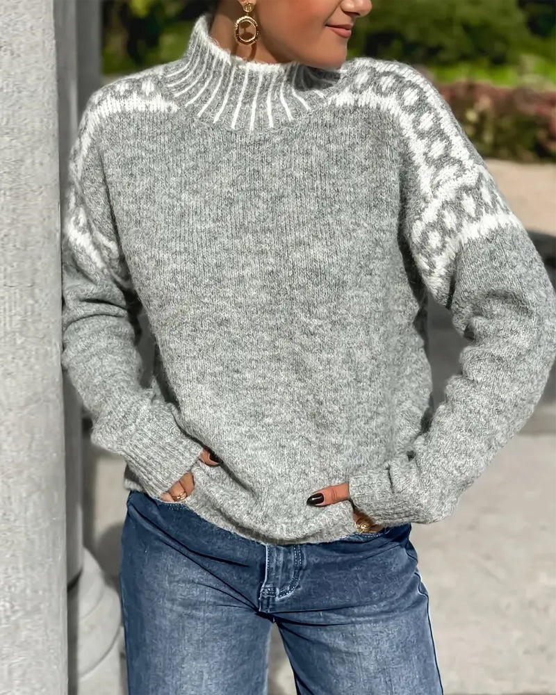 Grauer Strickpullover mit Stehkragen und weißem Zierstreifen über den Schultern, getragen zur Jeans vor einer Säule. 5