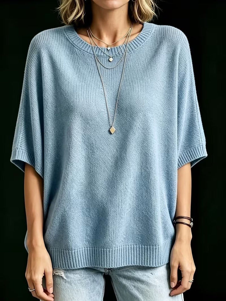 Frontansicht des hellblauen Strickoberteils mit kurzen Fledermausärmeln, gerade stehend getragen mit Halsketten und Armbändern. 16