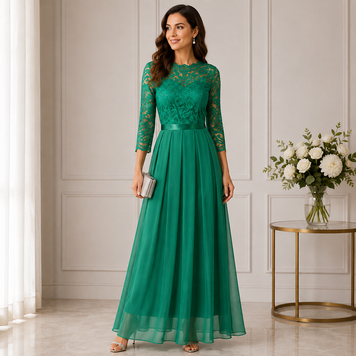 Smaragdgrünes Maxikleid mit Spitzenoberteil, Dreiviertelärmeln und Chiffonrock, getragen vor weißen Wandpaneelen neben 1