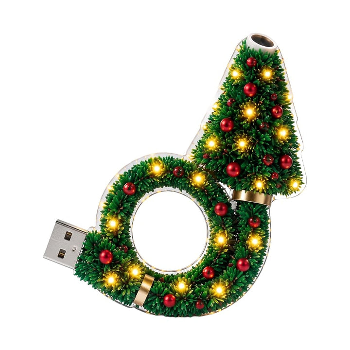 Freigestellte Produktansicht der Lampe: Tannenbaum mit rotem Schmuck auf einem Kranz, warm leuchtende LEDs, USB-Stecker links, Projektionsöffnung oben. 1