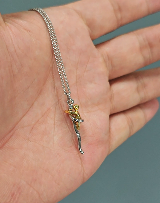Die Halskette mit dem kleinen silber-goldfarbenen Umarmungs-Anhänger liegt auf einer geöffneten Handfläche und zeigt so die Größe. 7