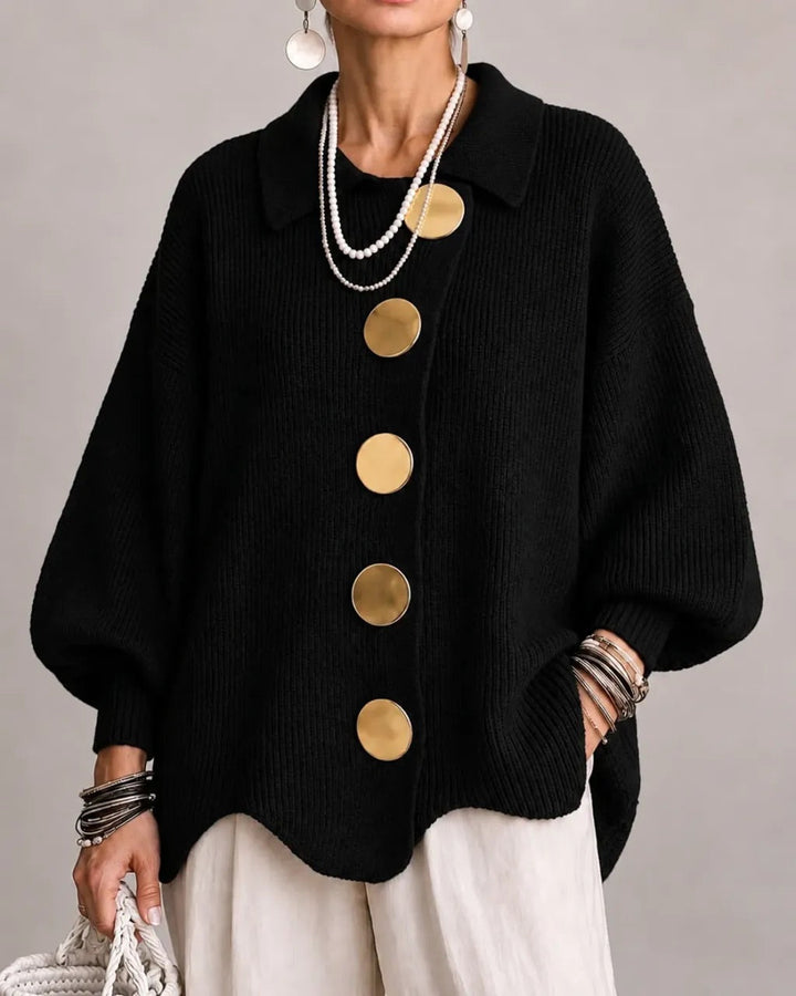 Frontansicht der schwarzen Strickjacke mit großen goldfarbenen Knöpfen, getragen zu weißer Hose und Perlenketten. 8