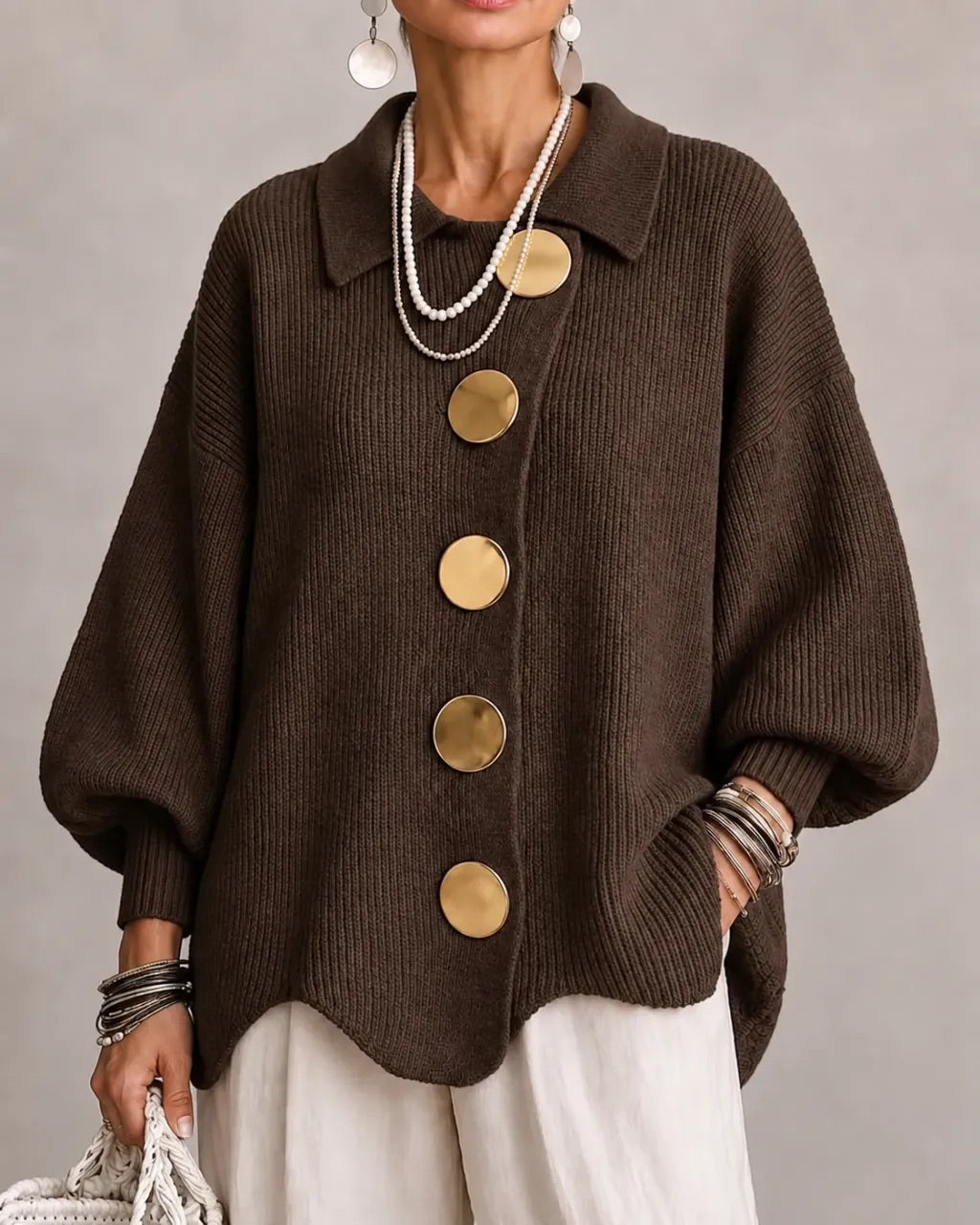Strickjacke in Dunkelbraun mit goldfarbenen Knöpfen, getragen zu weißer Hose, Perlenketten und Armreifen. 9