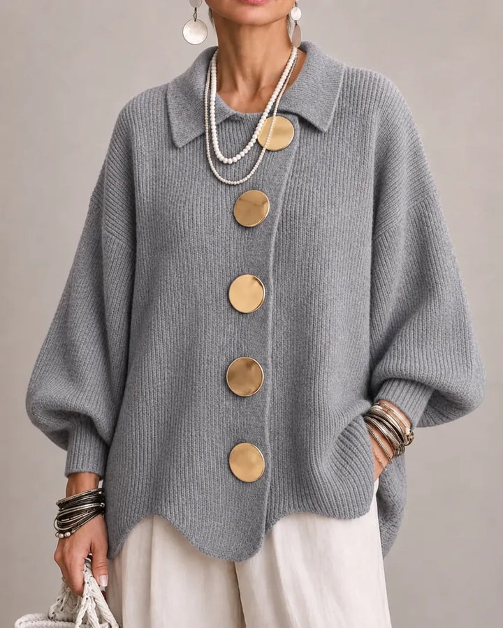 Strickjacke in mittlerem Grau mit goldfarbenen Knöpfen, getragen zu weißer Hose, Perlenketten und Armreifen. 18